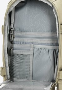 Šedý batoh uvnitř obsahuje několik zipových kapsiček, síťovou kapsu a zakřivený vzor na podšívce pro organizaci a texturu.