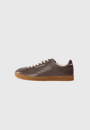Brown leather sneaker with a rounded toe, cream laces, and a gum rubber sole. Features stitching details and branding on the side and heel.