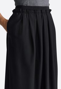 Pantaloni negri cu picioare largi, realizați dintr-un material moale, având o talie elastică strânsă și buzunare laterale, cu o textură netedă și pliseuri.