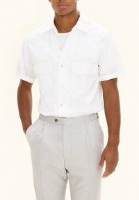 Korte mouw witte shirt met twee borstzakken en beige knopen, gecombineerd met lichtgrijze geplooide broek. gladde stofstructuur.
