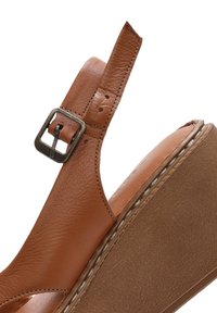 Sandaletta con tacco a zeppa in pelle marrone, caratterizzata da una fascia e una fibbia in metallo. Presenta una suola testurizzata e dettagli cuciti. Design con punta aperta.