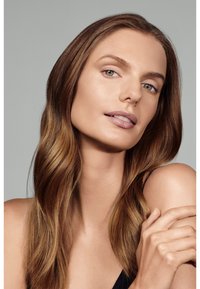 Retrato de una persona con cabello largo y ondulado de color castaño, maquillaje en tonos neutros y una blusa negra, que muestra una piel suave y una expresión natural.