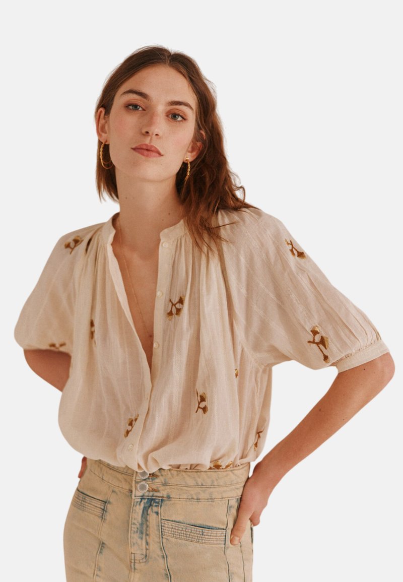 Cremefarvet bluse med korte pufærmer, knaplukning og delikat brunt blomsterbroderi. Sammen med højtsiddende lys blå denim.