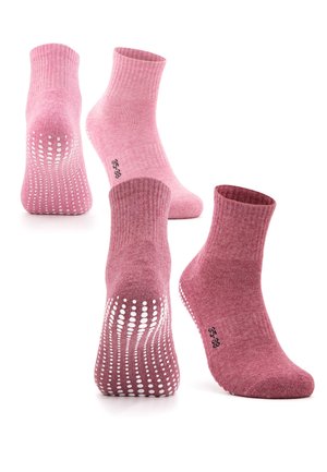 Feet wearing maroon non-slip grip socks with white dotted traction lines on soles, paired with black leggings against a white background.
