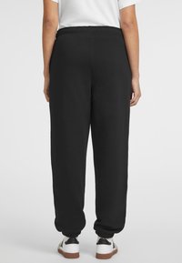 Zwarte sweatpants met een elastische tailleband, geribbelde boorden en een relaxte pasvorm, gecombineerd met witte sneakers met zwarte en bruine accenten.