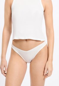 Witte ribgebreide string met een gladde tailleband en een ontwerp met minimale bedekking, gecombineerd met een bijpassend wit cropped tanktopje.