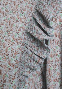 Hellblauer Stoff mit floraler Musterung in Braun und Grün, mit einem strukturierten, gerafften Rand für zusätzliche Details.