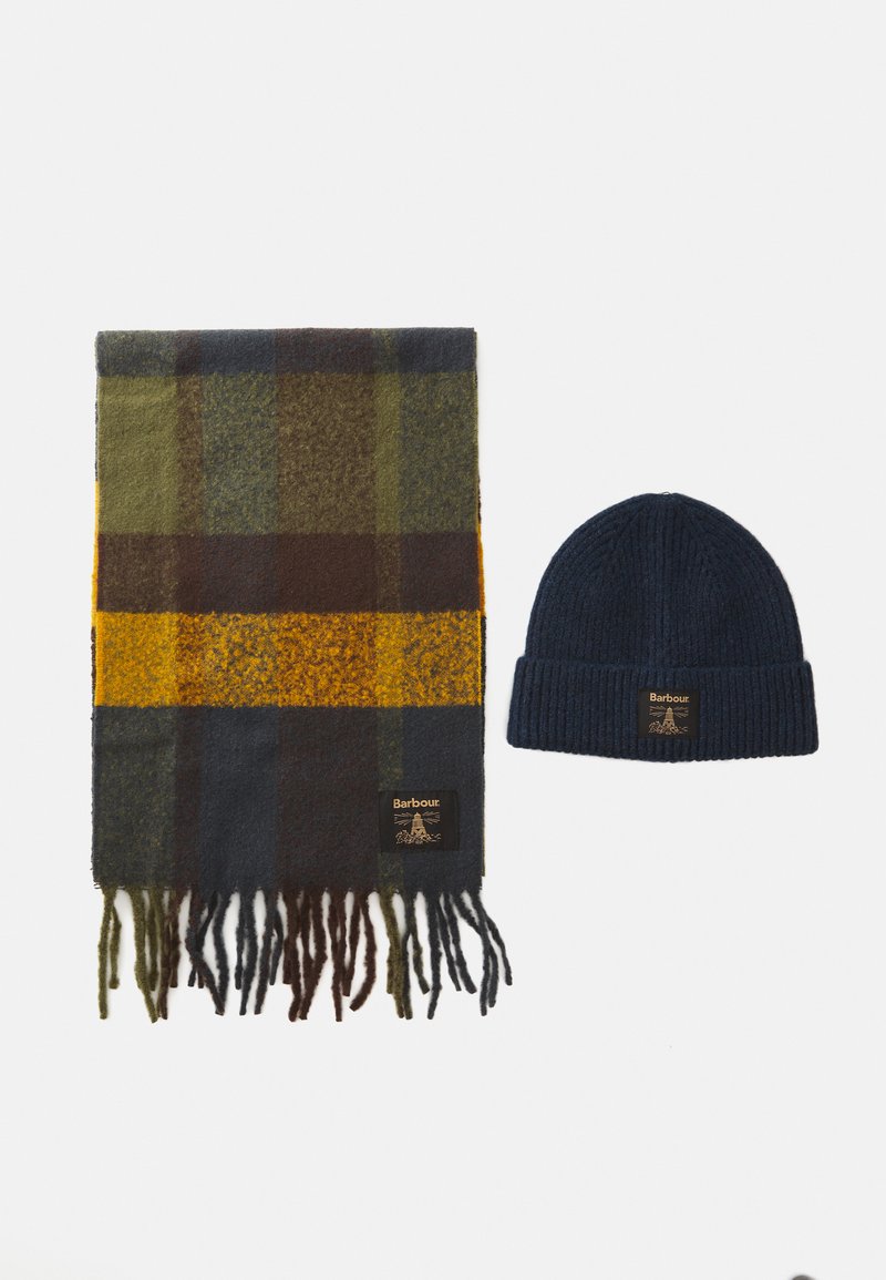 Grüner, brauner und gelber karierter Wollschal mit Fransen, neben einer marineblauen, gerippten Strickmütze, beide mit Barbour-Logopatches.