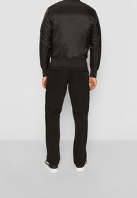 Chaqueta bomber negra con puños y cintura acanalados, combinada con pantalones cargo negros con bolsillos laterales, y zapatillas blancas.