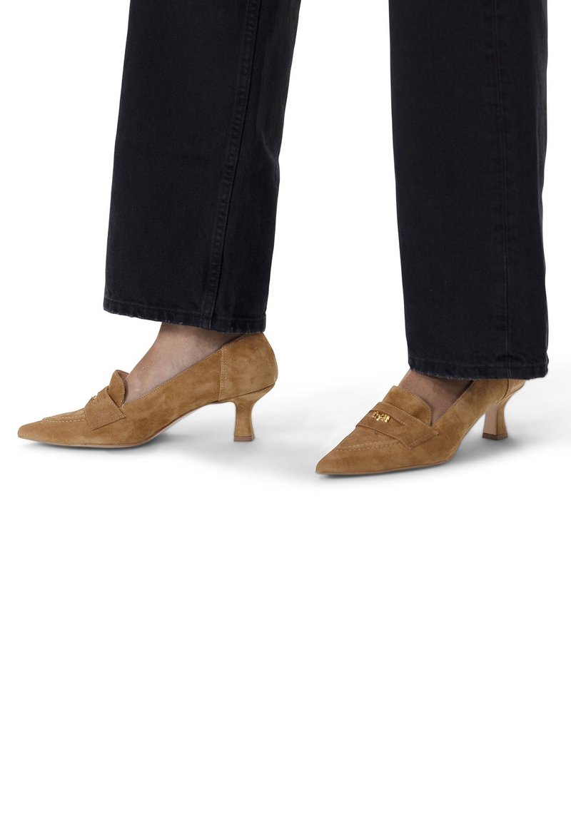 Scarpe con tacco alto in suede marrone, con punta affusolata, caratterizzate da un piccolo fiocco e un tacco basso a forma di kitten. Abbinato a pantaloni neri a gamba larga.