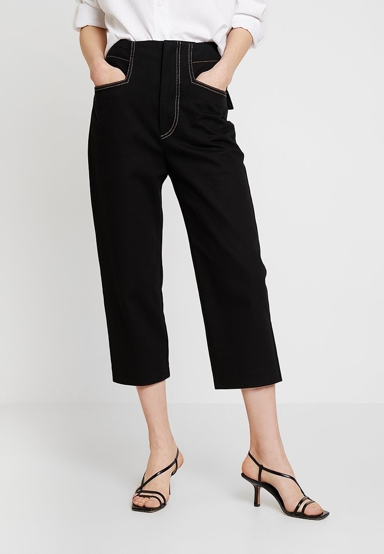 Pantalon noir court avec taille haute, doté de deux poches avant et de détails de coutures contrastantes. Assorti à des sandales noires à lanières.