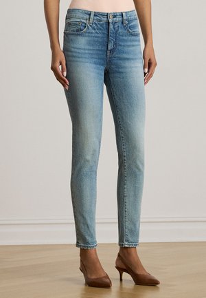 Helehallid teksapüksid, kitsas lõige, viie taskuga ja kulunud tekstuuriga. Lõpetatud nööbi ja luku sulgemisega, kantud pruunide kontsadega.