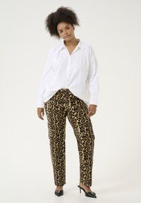 Witte button-up shirt gecombineerd met bruin luipaardprint broek, met een relaxte pasvorm en taps toelopende benen. Zwarte hakken maken de outfit compleet.