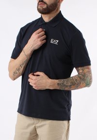 Polo azul marino en mezcla de algodón, con cuello de dos botones y logo EA7 en el pecho. Mangas cortas con un corte entallado.