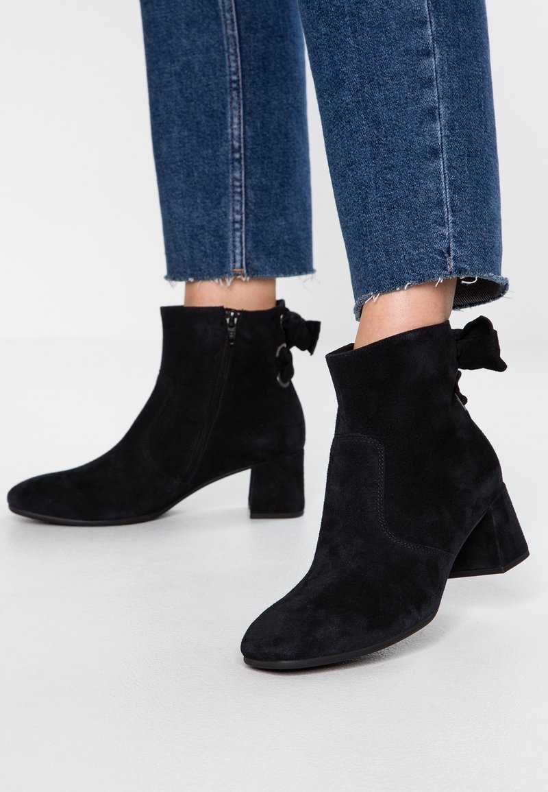 Bottes noires en daim à talons carrés avec fermetures éclair latérales portées avec un jean bleu délavé raccourci.