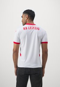 Balta RB Leipzig marškinėliai su raudonais akcentais, trumpomis rankovėmis, apvaliu kaklu ir užrašu "RB LEIPZIG" ant nugaros. Lygi, sportinė medžiaga.
