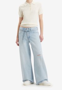 Ljusblå vida jeans i denim med fransade detaljer och slitage. Matchas med en krämfärgad kortärmad polo.