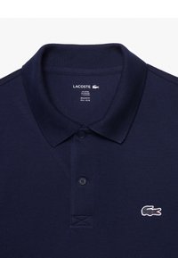 Polo en bleu marine en coton et élasthanne. Il présente un col en côtes, une patte de boutonnage à trois boutons et un logo brodé sur la poitrine.
