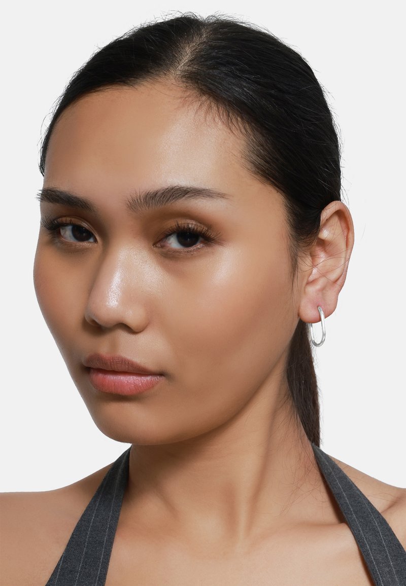 L'orecchino a cerchio d'argento presenta un design liscio e arrotondato. Il modello ha capelli neri lisci e un tono della pelle neutro, che mette in risalto l'accessorio.