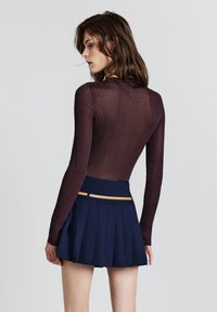 Top a maniche lunghe ribbed color bordeaux abbinato a una gonna plissettata blu navy con un dettaglio tan in vita. Texture complessiva liscia.