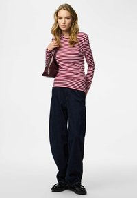 Langärmliges, rot-weiß gestreiftes Oberteil kombiniert mit weit geschnittenen, dunkelblauen Jeans. Das Modell hält eine dunkle Tasche und trägt glänzende schwarze Schuhe.