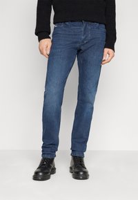 Dunkelblaue Jeans im Slim-Fit-Schnitt, aus Denim gefertigt. Verfügt über fünf Taschen und dezente Nähte. Getragen mit schwarzen Schnürstiefeln.