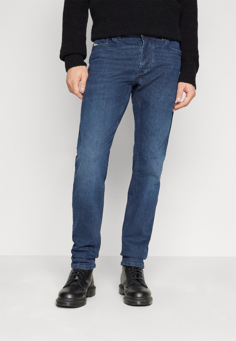 Dunkelblaue Jeans im Slim-Fit-Schnitt, aus Denim gefertigt. Verfügt über fünf Taschen und dezente Nähte. Getragen mit schwarzen Schnürstiefeln.