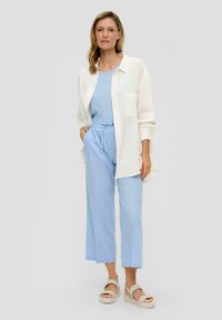 Witte button-up shirt over een lichtblauw tanktop, gecombineerd met lichtblauwe, losvallende, cropped broek en beige platform sandalen.