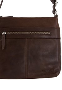 Bruin leren schoudertas met een voorzak met ritssluiting, subtiele stikseldetails en een merkaanzegging rechtsonder.