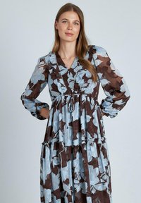 Vestido floral con un patrón azul y marrón, escote fruncido, mangas largas y falda tipo volante hecha de tela ligera.