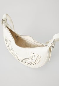 Weiße Leder-Schultertasche mit perforiertem Design, geschwungener Form, Reißverschluss und verstellbarem Tragegurt. Das Innenfutter ist glatt und hell.