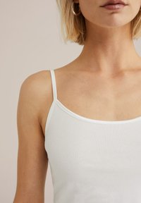 Valge tank top õhukeste rihmadega, ümmarguse kaelusega ja siledast, kergest kangast tekstuuriga. Õmblused on korralikult viimistletud.