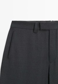 Pantalon gris foncé sur mesure avec une texture lisse, doté de poches latérales et d'une ceinture nette avec passants pour ceinture et plis avant.