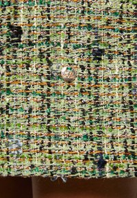 Tissu tweed vert, noir, blanc et or étroitement tissé avec un petit bouton rond doré au centre.