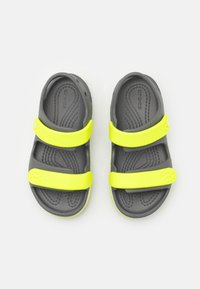 Mustat sandaalit, joissa on kaksi leveää keltaista remmiä. Valmistettu kestävästä materiaalista, jossa on teksturoitu pohja ja avoin muotoilu ilmanvaihtoa varten.