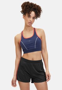 Sujeta de deportes en color azul marino con acentos en coral y costuras blancas, combinada con pantalones cortos atléticos negros que tienen una cinturilla elástica y un corte holgado.