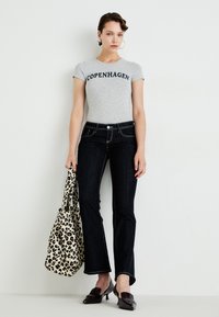 Grå tettsittende t-skjorte med teksten "COPENHAGEN", mørke vide jeans, veske med tigermønster og mørke hæler, satt mot en nøytral bakgrunn.