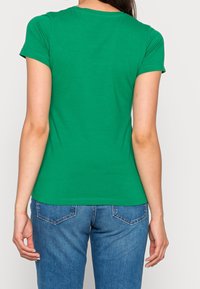 Grünes T-Shirt mit kurzen Ärmeln und rundem Ausschnitt, aus weicher Baumwolle, taillierte Passform, kombiniert mit blauen Jeans.