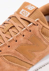 Vaaleanruskea mokkanahkainen tennari hengittävällä verkkokankaalla, jossa on ruskeat nauhat, valkoinen pohja ja suuri "N"-logo sivulla. Mallinumero 420 kielen kohdalla.