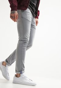 Vaqueros de mezclilla gris claro con un corte slim, que cuentan con un dobladillo enrollado y un ligero desgaste, combinados con zapatillas blancas y una chaqueta bomber burdeos.