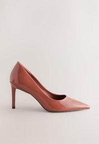 Cipele s visokim potpeticama i špicastim vrhom u sjajnoj koraljnoj lakiranoj koži. Odlikuje ih elegantan dizajn sa vitkom štiklom i glatkom teksturom.