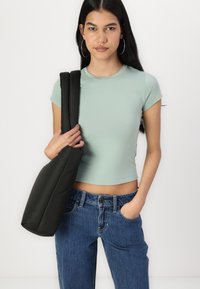 Bluză scurtă, ajustată, de un verde deschis; blugi albaștri cu talie înaltă; ținând o poșetă întunecată, din material matlasat, cu curele groase.