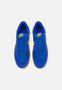 Sinised Nike spordi jalatsid kollaste elementidega, pehme võrgusilma ja nahast materjal, sirged paelad, ümmargune varvas ja kummist välistald. Ülevalt vaade.