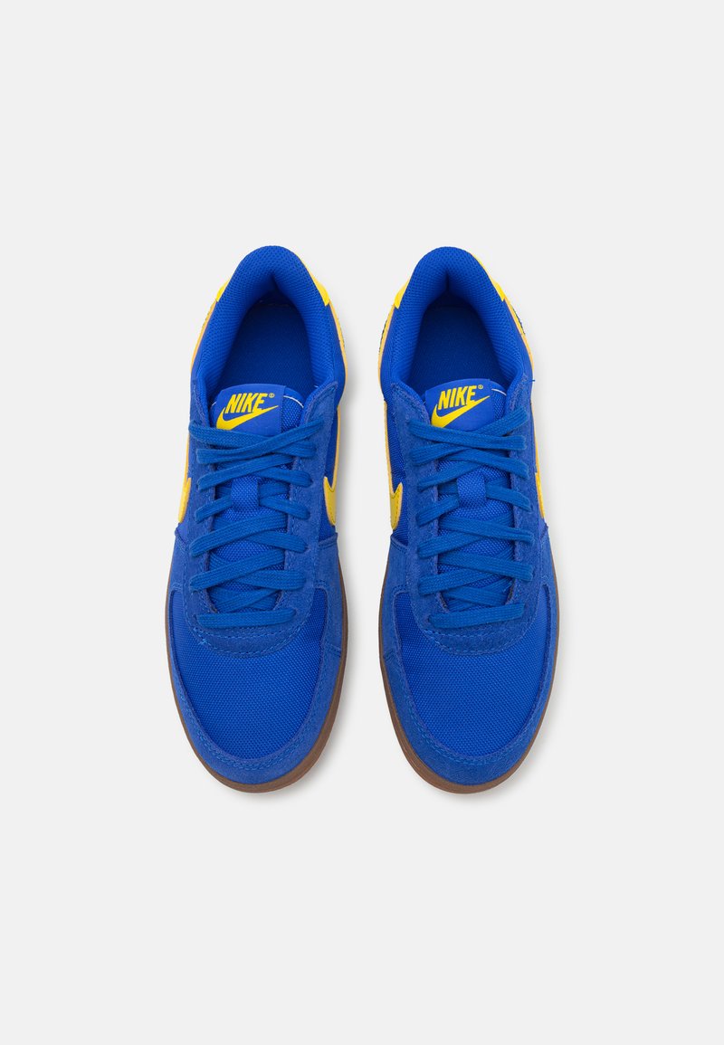 Zapatillas Nike azules con acentos amarillos, material de malla y ante, cordones planos, punta redonda y suela de goma. Vista desde arriba.