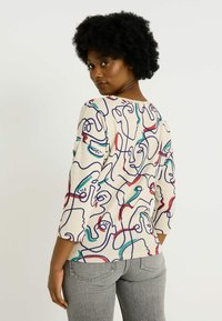 Haut à motif de lignes abstraites multicolores en tissu léger beige. Il présente un col rond et des manches trois-quarts.