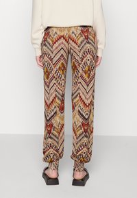 Pantalons à motif avec un imprimé géométrique multicolore dans des tons terreux, avec des poignets élastiques et une coupe décontractée. Complétés par des sandales noires.