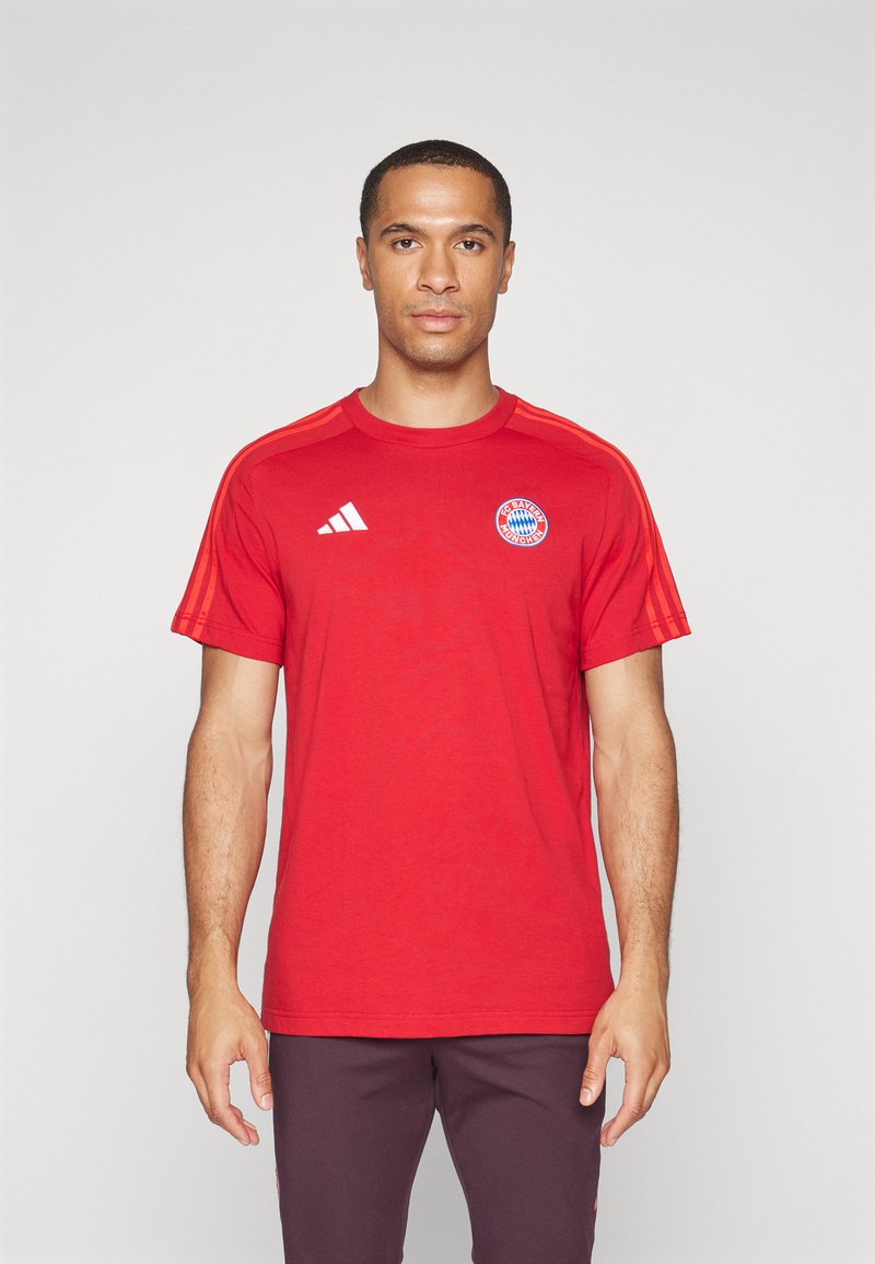 Rød treningst-skjorte laget av myk stoff. Har hvit Adidas-logo og Bayern München-emblem på brystet, med oransje striper på skuldrene.