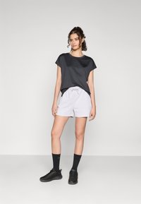 Maglietta a maniche corte grigia scura, pantaloni corti grigi chiari con coulisse, calzini neri e sneaker nere. Tessuti morbidi e vestibilità rilassata.