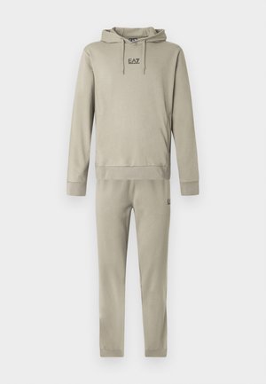 Beežis värvitoonis kapuutsiga dressipluusi ja dressipükste komplekt. Pehme kangas, soonikkätised ja -vöökoht. Rinnal ja säärel väike logo.