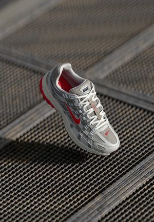 Nike tekaš je obutvena od neoprena, ki ima sivo mrežasto zgornji del, rdeče detajle, debel podplat in vezalne podrobnosti. Teksturna površina pod čevljem.
